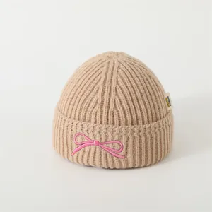 Detail of khaki cable knit baby hat with pink bow embroidery and Didicute woven label