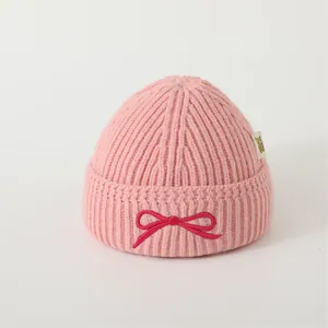 Detail of pink knitted beanie featuring a fuchsia bow embroidery and branded side label