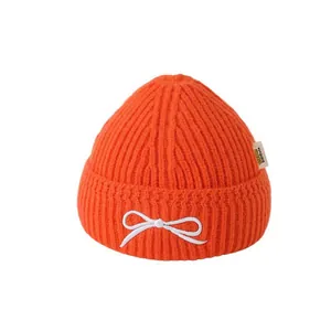 Bright orange knit beanie for toddlers featuring a white bow and ribbed texture