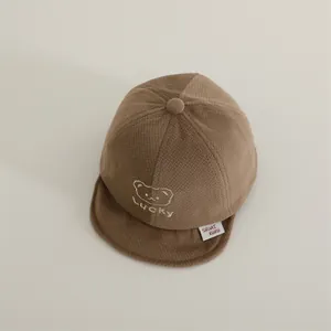 Detail of baby winter baseball cap featuring Lucky embroidery and bear icon on brown fabric