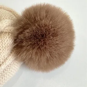 Detailed close-up of a large fluffy brown pom-pom on a thick beige knit winter hat