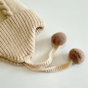 Close-up of beige knit baby hat featuring ribbed texture and dark brown fuzzy pom-poms