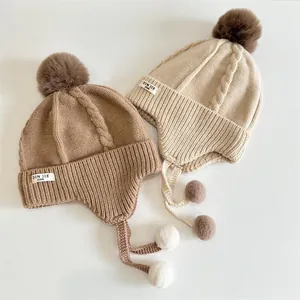 Close-up of thick cable knit pattern and fluffy faux fur pom-poms on winter earflap hats