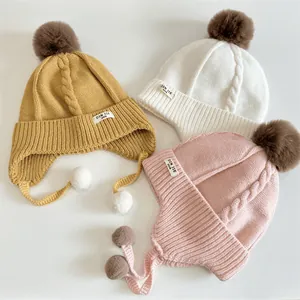 Winter knit baby beanie with ear flaps and pom-poms in yellow, cream, and pink colors