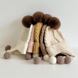 Close-up of winter knit hats with large fur pompoms and braided earflap cords in multi colors