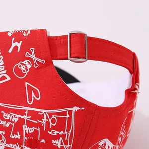 Detailed close-up of a red kids' baseball cap featuring white graffiti print and metal buckle