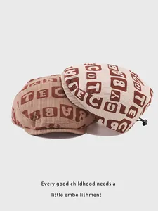 Detail of corduroy baby berets showing letter prints and adjustable drawstring toggles