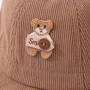 Detailed close-up of brown corduroy kid bucket hat with knitted bear patch and button