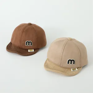 Detail of brown and beige baby baseball caps with corduroy brim and letter M patch
