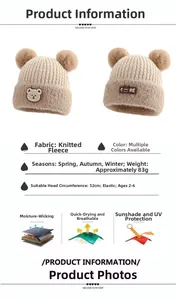 Detailed view of child's cream knit beanie with dual faux fur pom-poms and bear patch