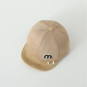 Detail of baby baseball cap featuring suede fabric with corduroy brim and m-letter patch