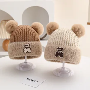 Detail of baby winter knit hats with double pom-poms and furry trim on a white display