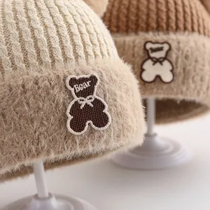 Detailed view of winter knitted baby hat with bear patch and plush pom-poms