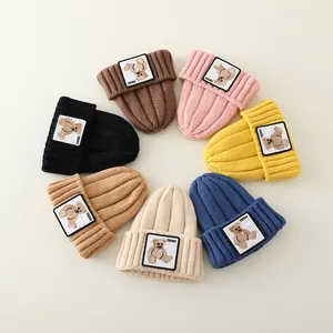 Flat lay of colorful knit beanies with cute teddy bear labels in various winter shades