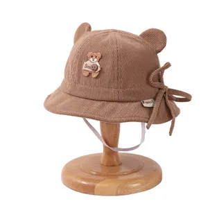 Brown corduroy baby bucket hat with bear ears and chin strap on a wooden stand
