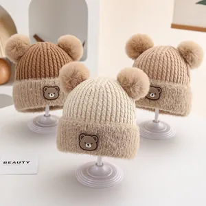 Close-up of knit winter hats with fluffy double pom-poms and cartoon bear patches