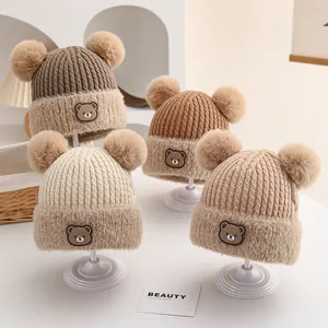 Detailed view of knitted winter beanies for babies with double fur pom-poms in earth tones