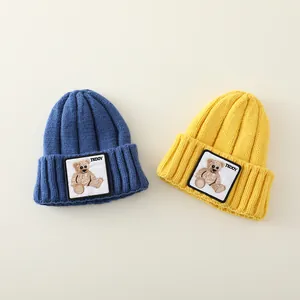 Close-up of thick knit winter beanies in blue and yellow with Teddy bear patch detail