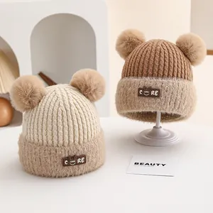 Detail of baby winter knit hat with double pompoms and embroidered patch on soft fabric