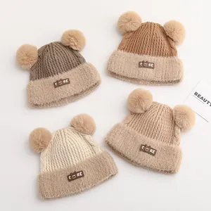 Close-up of knit baby hats with dual fur pom-poms and CORE smile patches in earth tones