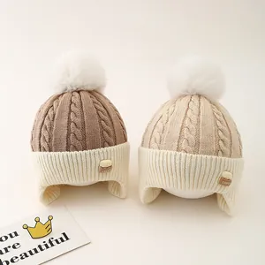 Close-up of winter knit ear-flap hats in coffee and beige with fluffy white pom-poms