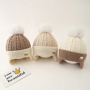 Detailed cable knit texture of children's winter earflap hats with fluffy white pom-poms