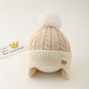 Close-up of cable knit earflap hat for kids featuring a large white faux fur pompom