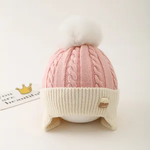 Detail of pink knit baby hat featuring plush white pompom and soft fleece earflaps