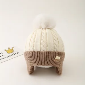 Detail of knit child hat with pompom ear flaps and Choco biscuit patch decoration