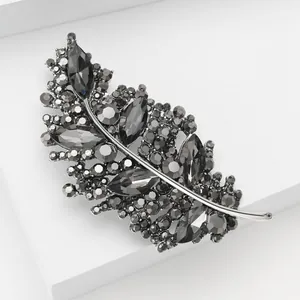 Eleganter Blatt-Anstecker mit dunklen Kristallen und Metall-Finish auf weißem Podest