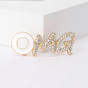 Detail of OMG brooch with gold metal, white enamel and sparkling inlaid rhinestones