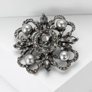 Baroque floral brooch with grey faceted crystal and pearls on a white geometric stand