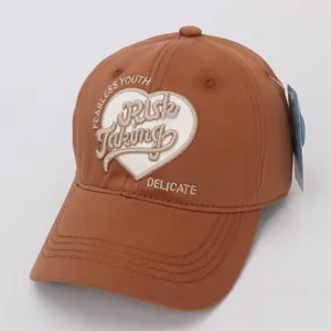Détail d'une casquette marron foncé avec broderie cœur blanc et texte Fearless Youth