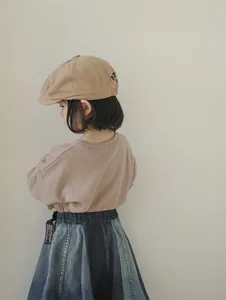 Detailed side view of khaki newsboy cap and patchwork denim skirt on a child model