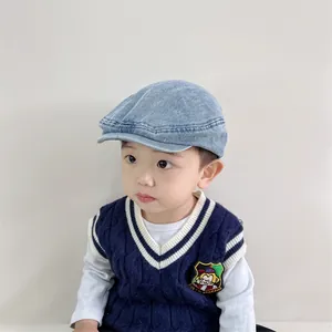 Détail d'une casquette en denim bleu clair et d'un gilet en tricot bleu marine à écussons