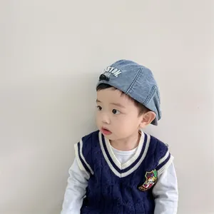 Détail du béret en denim pour bébé avec broderie BOSTON et gilet en maille bleue