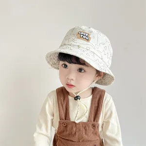 Child in beige cotton sun hat with dinosaur pattern and LOVE YOU label for summer
