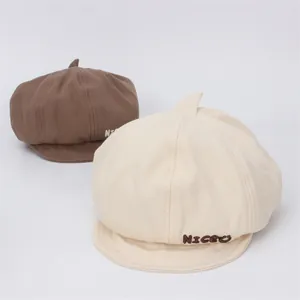 Détail du lettrage brodé NICEU sur des bérets en coton de couleurs marron et crème