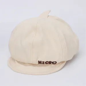 Détail de béret en toile pour bébé crème avec broderie Niceu et motif visage souriant