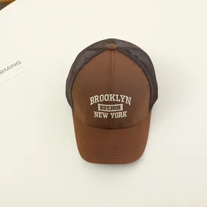 Close-up of brown Brooklyn mesh trucker hat with white embroidery on cream background