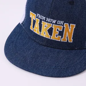 Detailed close-up of TAKEN embroidery on navy denim and white mesh trucker hat