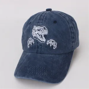 Détail d'une casquette en denim délavé bleu marine avec broderie de dinosaure blanc