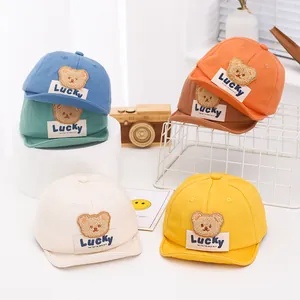 Detail view of multi-color baby baseball caps featuring plush bear patches and woven labels