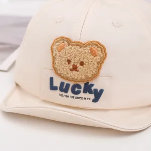Detail of baby baseball cap featuring 3D fuzzy bear patch and Lucky label on cream fabric