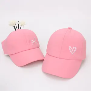Détail de casquette rose pour queue de cheval avec broderie cœur et nœud blanc