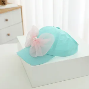Detail of mint green girls visor cap featuring large pink bow and pearl decorations