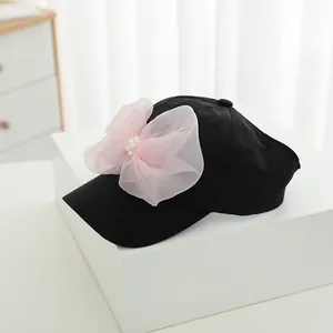 Detail of a black baseball cap with a large pink mesh bow and white pearl embellishments