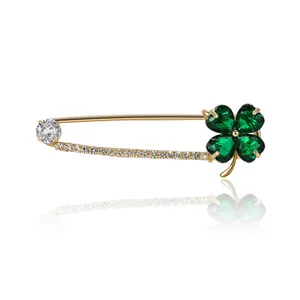 Golden clover safety pin brooch with green crystals and sparkling zircons on white base