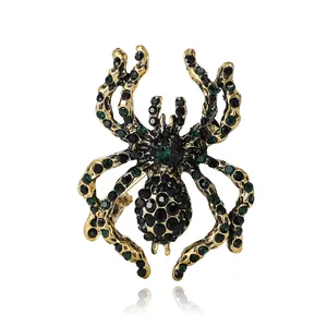 Vintage gold spider brooch with black and green rhinestones on reflective white background