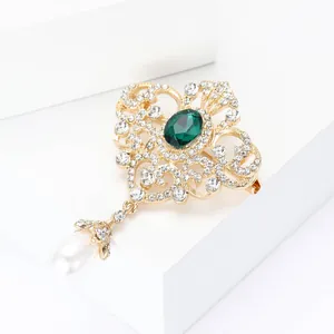 Detalle macro de broche vintage dorado con gema verde esmeralda y colgante de perla